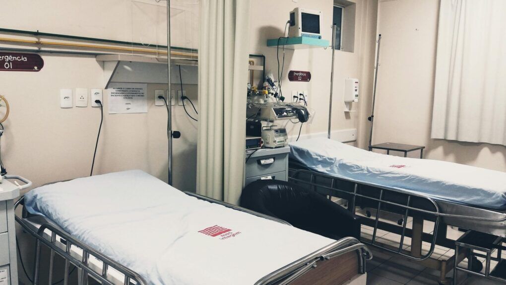 Empty hospital room with two patient beds, medical monitors, privacy curtains, and equipment on shelves
