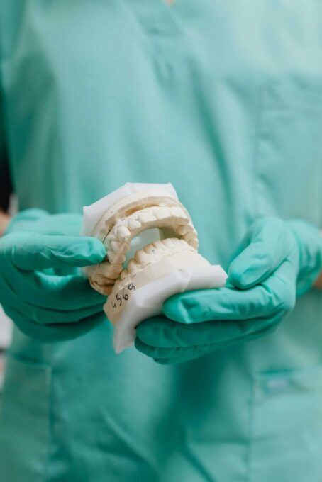 A dental professional in green scrubs and gloves holds up a white plaster dental mold model