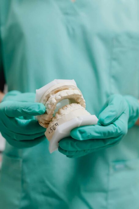A dental professional in green scrubs and gloves holds up a white plaster dental mold model