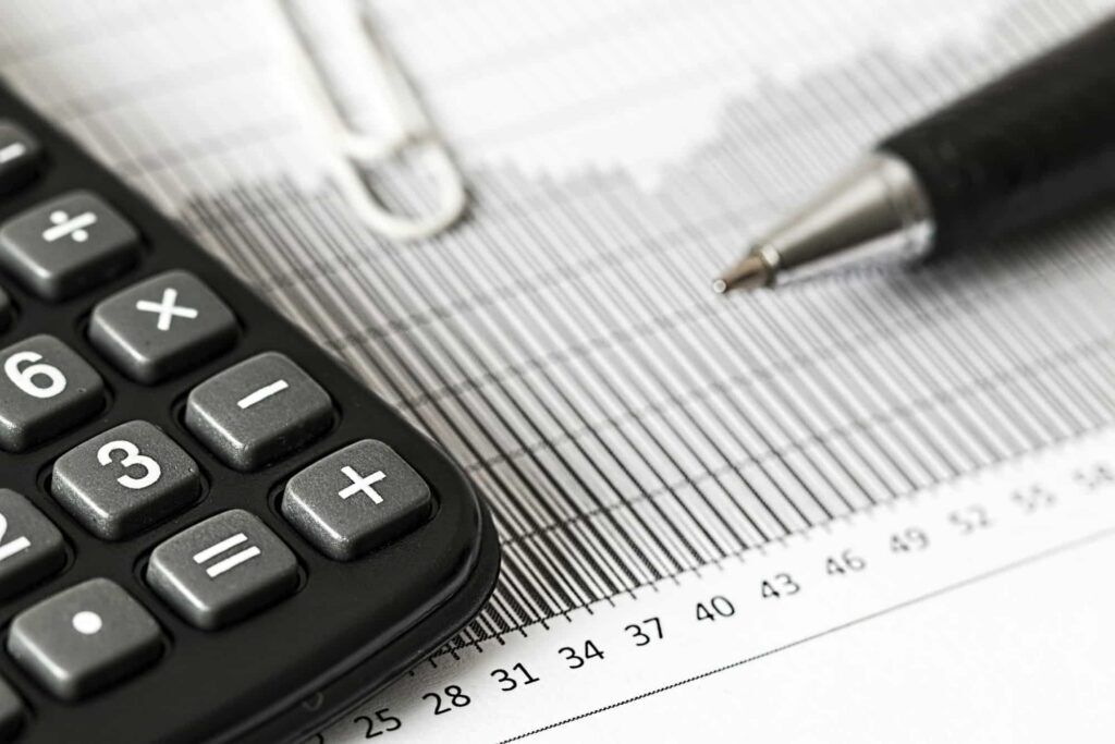 A calculator, pen, and paperclip resting on financial ledger paper with columns and numbers