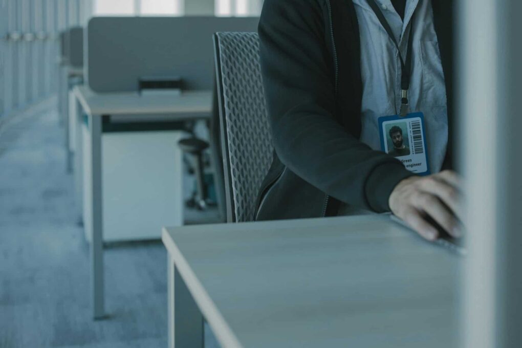 A person wearing an ID badge sitting at a desk in an office with rows of empty cubicles